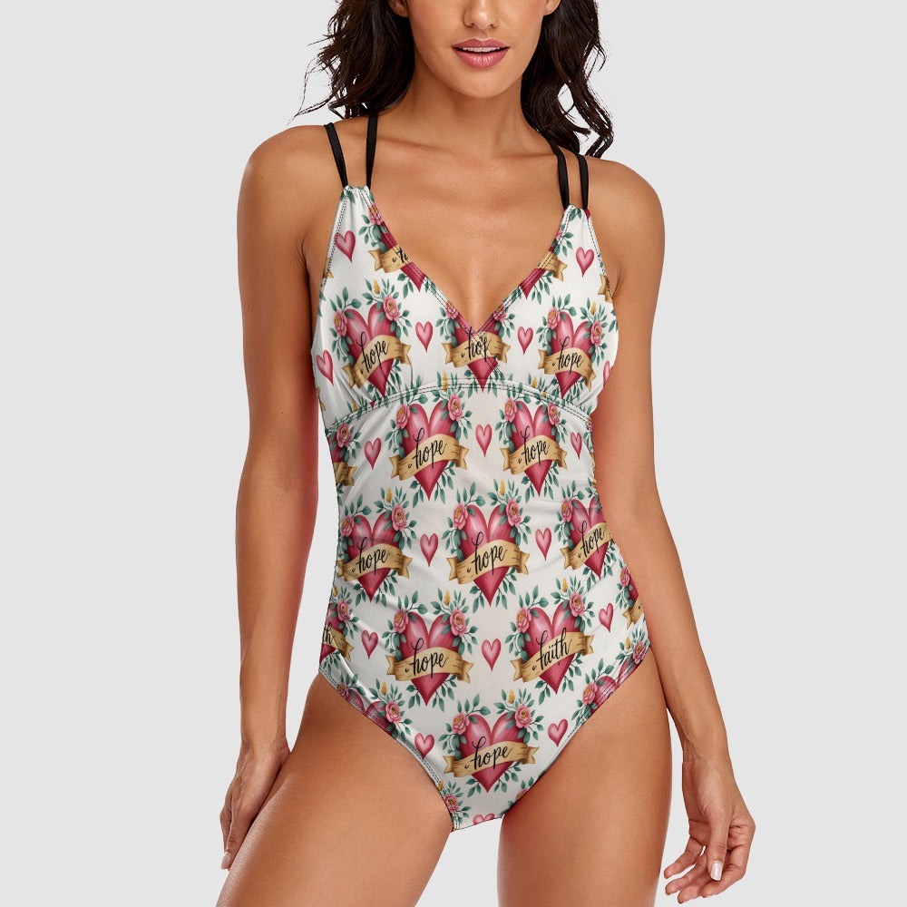 White one-piece swimsuit with a tattoo-style rose and heart pattern, banners reading "faith" and "hope," and a deep V-neck with double black straps.